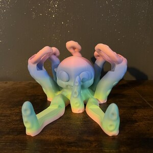 Könnte beinhalten: Eine regenbogenfarbene Oktopus-Figur mit einem niedlichen Gesicht und acht Tentakeln. Der Oktopus ist aus einem glatten, plastikähnlichen Material gefertigt und ist eine lustige und skurrile Dekoration.