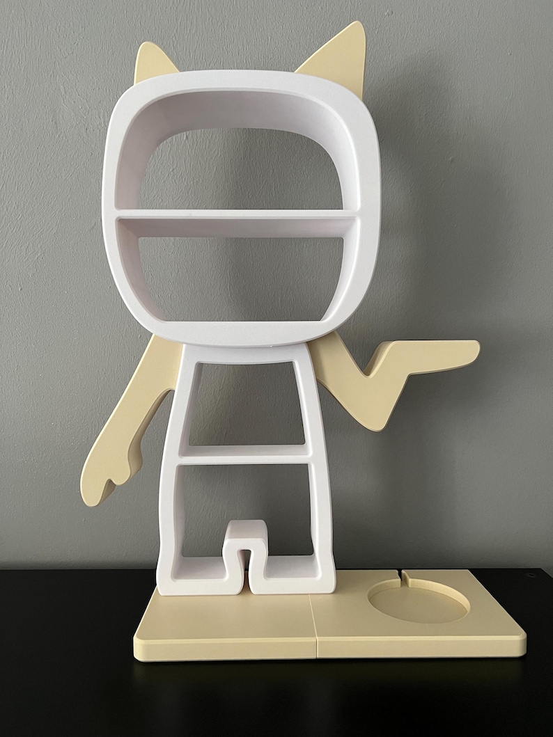 May include: White and beige shelf unit shaped like a cartoon character with cat ears. The shelf has multiple shelves and a small circular platform at the base.