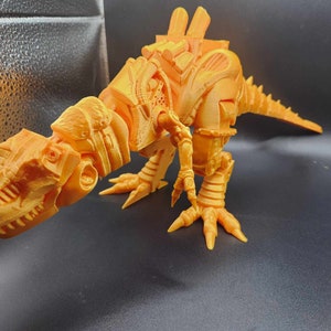Puede incluir: Un modelo de dinosaurio naranja impreso en 3D con un diseño mecánico detallado. El dinosaurio está en posición de caminar con la cabeza girada hacia un lado.