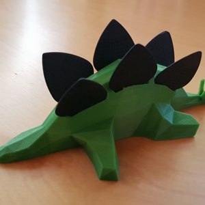 Może przedstawiać: Zielona zabawka dinozaura wydrukowana w 3D z czarnymi kolcami na grzbiecie. Dinozaur leży na boku, ogon skierowany w prawo.