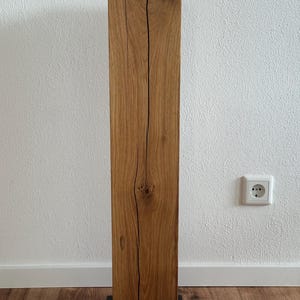May include: A tall, rectangular wooden pedestal with a natural wood finish and a black metal base. The wood has a unique grain pattern and knots.