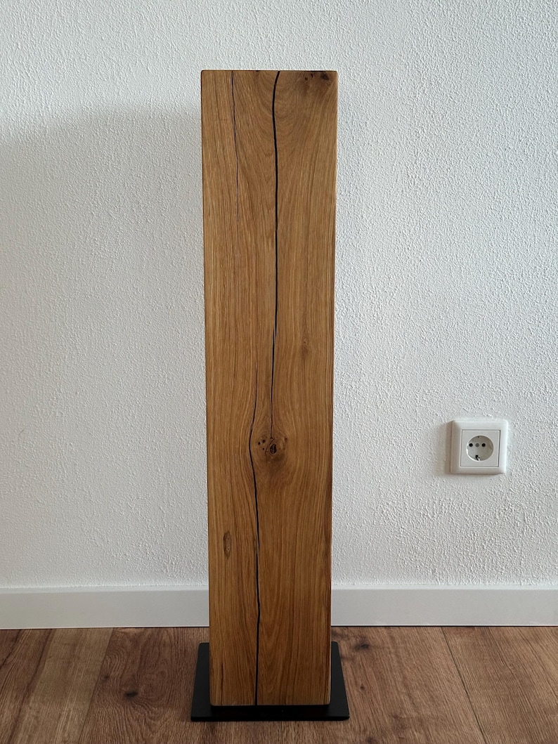May include: A tall, rectangular wooden pedestal with a natural wood finish and a black metal base. The wood has a unique grain pattern and knots.