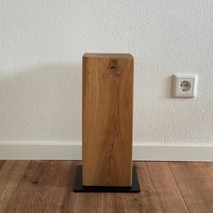 May include: A wooden pedestal with a natural wood finish and a black metal base. The pedestal is square and has a rustic look.