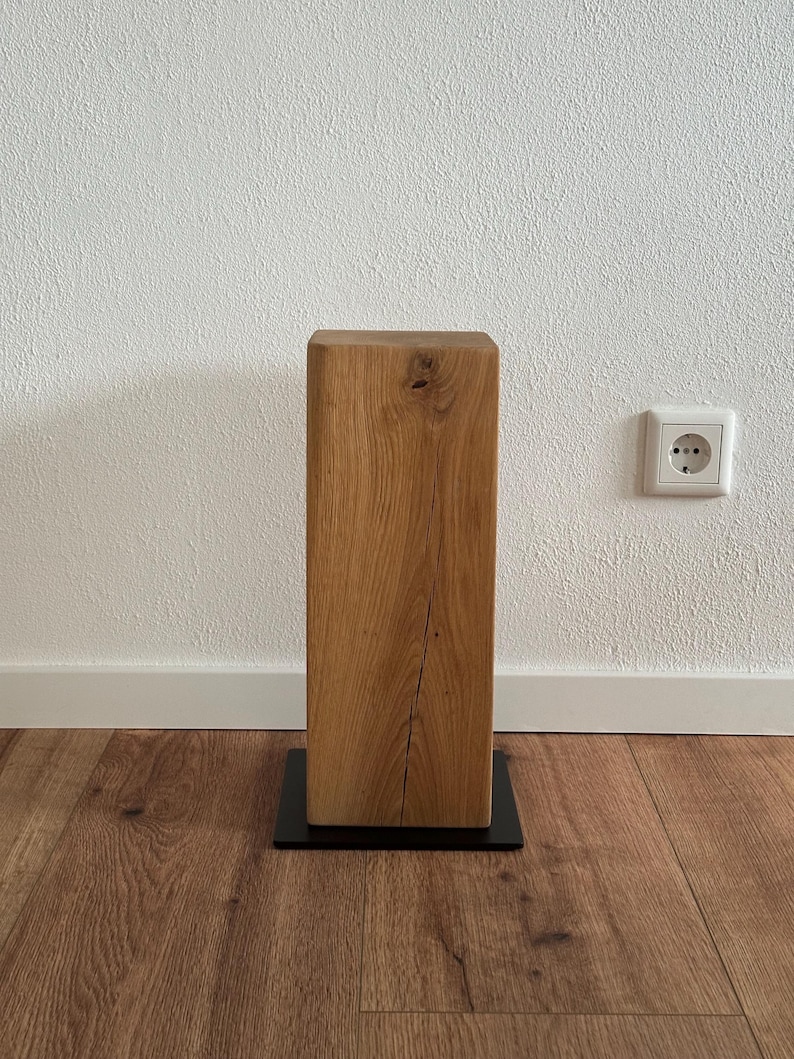 May include: A wooden pedestal with a natural wood finish and a black metal base. The pedestal is square and has a rustic look.