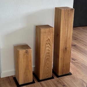 May include: Three wooden blocks of varying heights, each with a dark brown base. The blocks are made of natural wood with a light brown color and a visible grain pattern.