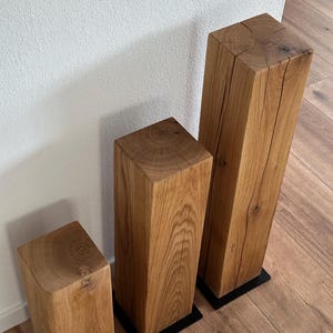 May include: Three wooden blocks of varying sizes, each with a natural wood finish and a dark brown base. The blocks are arranged in a row from smallest to largest.