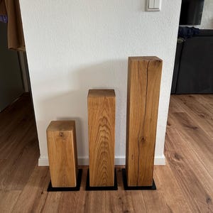 May include: Three wooden blocks of varying sizes, each with a natural wood finish and a black base. The blocks are arranged in a row from smallest to largest.