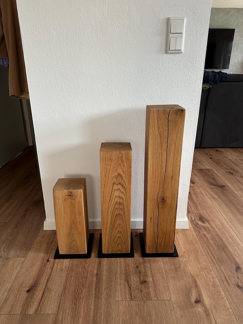 May include: Three wooden blocks of varying sizes, each with a natural wood finish and a black base. The blocks are arranged in a row from smallest to largest.