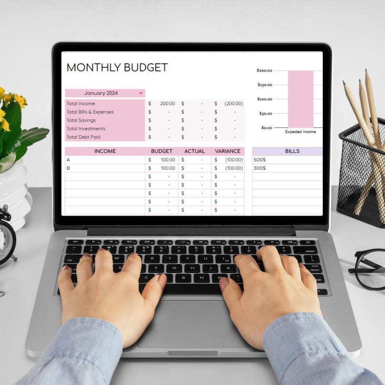 May include: A laptop computer displaying a monthly budget spreadsheet with categories for income, budget, actual, variance, and bills. The spreadsheet includes a bar graph showing expected income. The laptop is on a white surface with a person's hands typing on the keyboard.