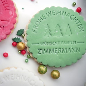 Könnte beinhalten: Drei dekorierte Weihnachtskekse mit grünem, weißem und rotem Zuckerguss. Der grüne Keks hat den Text "Frohe Weihnachten" und "wünscht Familie Zimmermann" in weiß. Der weiße Keks hat den Text "Frohe Weihnachten" in schwarz. Der rote Keks hat den Text "Familie Zimmermann" in weiß.