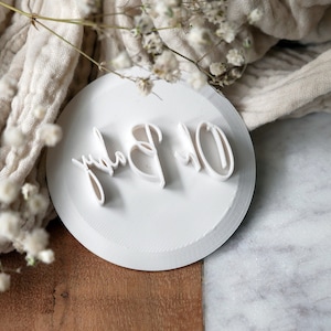 May include: White round cake topper with the words "Oh Baby" in a cursive font.