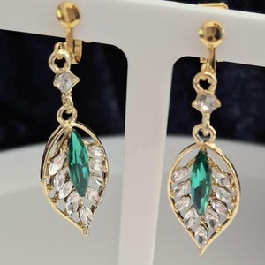 May include: A pair of gold tone clip-on earrings with a green marquise shaped stone surrounded by clear rhinestones in a leaf design.