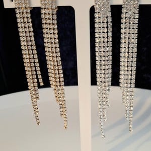 May include: Two pairs of long, dangling earrings with multiple strands of clear rhinestones. One pair has gold-toned metal and the other has silver-toned metal.