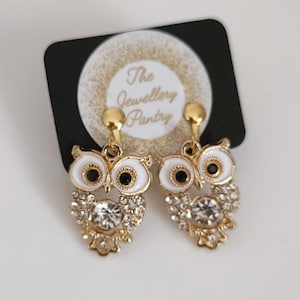May include: Gold owl earrings with white enamel and clear rhinestones. The earrings are clip-on style and feature the text "The Jewellery Pantry".