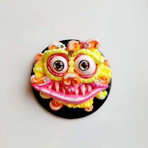 Puede incluir: Una escultura de arcilla colorida, caprichosa y detallada de un monstruo con ojos grandes, una boca ancha y un fondo negro.