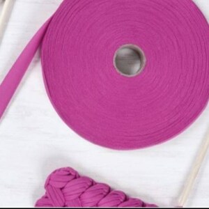 May include: A roll of pink cotton rope yarn with a wooden dowel rod. The yarn is wound around a cardboard tube.