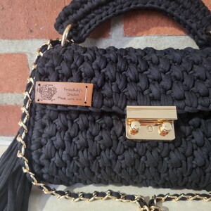 May include: Black crocheted handbag with a gold chain strap and a brown leather tag that reads "Frankly's Crochet Made with Love".