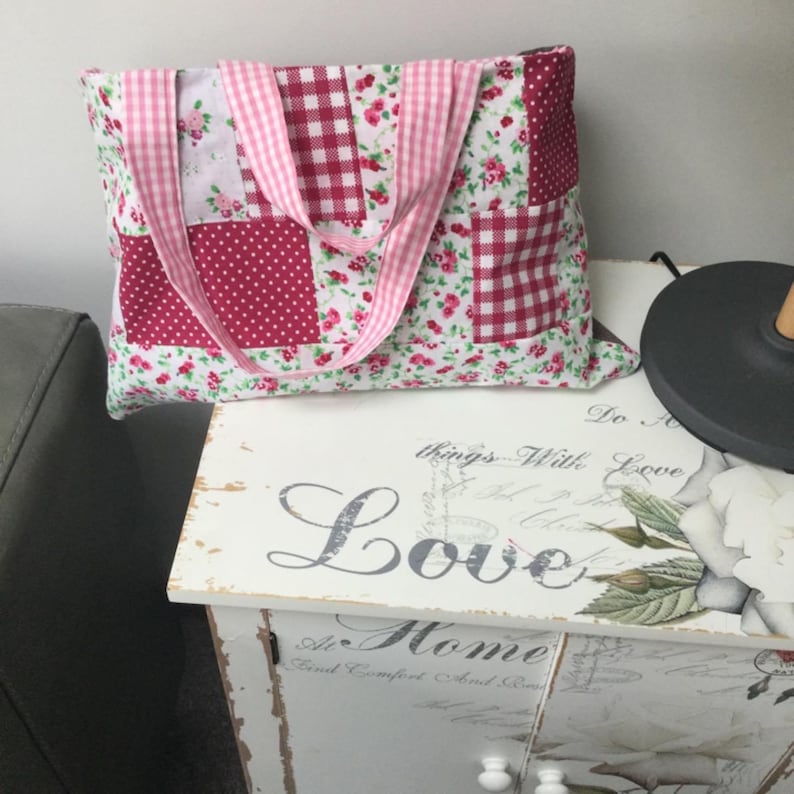 May include: A patchwork tote bag with pink and red floral patterns and gingham fabric. The bag has pink and white ribbon straps.
