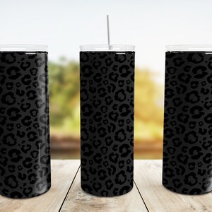 May include: Three stainless steel tumblers with black leopard print designs. The tumblers are on a wooden surface with a blurred background.