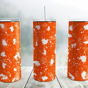May include: Three orange and white stainless steel tumblers with white splatter paint design. The tumblers have black lids and white straws.