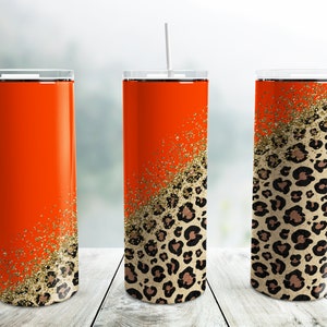 Pode incluir: Três copos de aço inoxidável com um design de estampa de leopardo e glitter dourado. Os copos são laranja, com a estampa de leopardo e o glitter dourado na metade inferior dos copos.