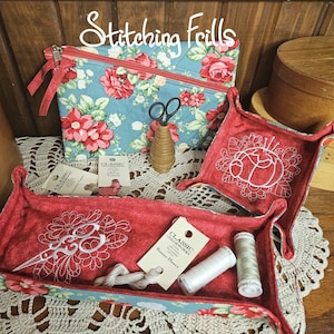 May include: Two red fabric trays with white embroidery of scissors and a flower. The trays are filled with embroidery floss and a spool of thread. The trays are sitting on a crocheted doily. The text "Classic Crafworks" and "Bunny Honey" are visible on the labels.