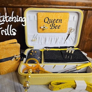 May include: Yellow sewing kit with a black and yellow fabric design. The kit is open and contains various sewing supplies, including needles, thread, scissors, and a measuring tape. The kit also has a small fabric pouch with the words "Queen Bee" embroidered on it.