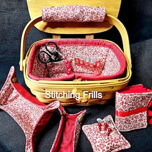 May include: A wooden sewing basket with a red floral fabric lining and handle. The basket contains sewing tools, including scissors and clips. The text "Stitching Frills" is visible on the basket.