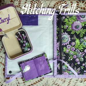 May include: A purple and black floral print sewing kit with a zippered closure, open to reveal a needle case, pin cushion, and a small jewelry box with the name "Cheryl" inside. The kit includes a variety of sewing pins and needles.