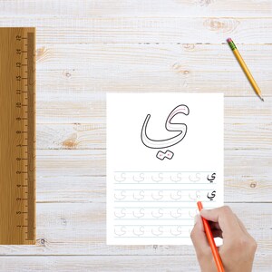 May include: A worksheet with a large Arabic letter 'Y' printed in black. The letter is outlined in pink. Below the letter are multiple lines with the letter 'Y' printed in gray. A hand is holding a red pencil and tracing over the letter 'Y' on the worksheet.
