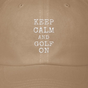 May include: A tan baseball cap with the text "KEEP CALM AND GOLF ON" in white. The cap has a curved brim and a structured crown. The hat is a classic style, suitable for golf enthusiasts.