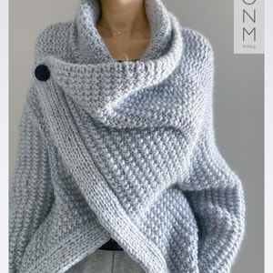 May include: A light grey knitted sweater with a large cowl neck and a single button closure. The sweater has a relaxed fit and a slightly cropped length.