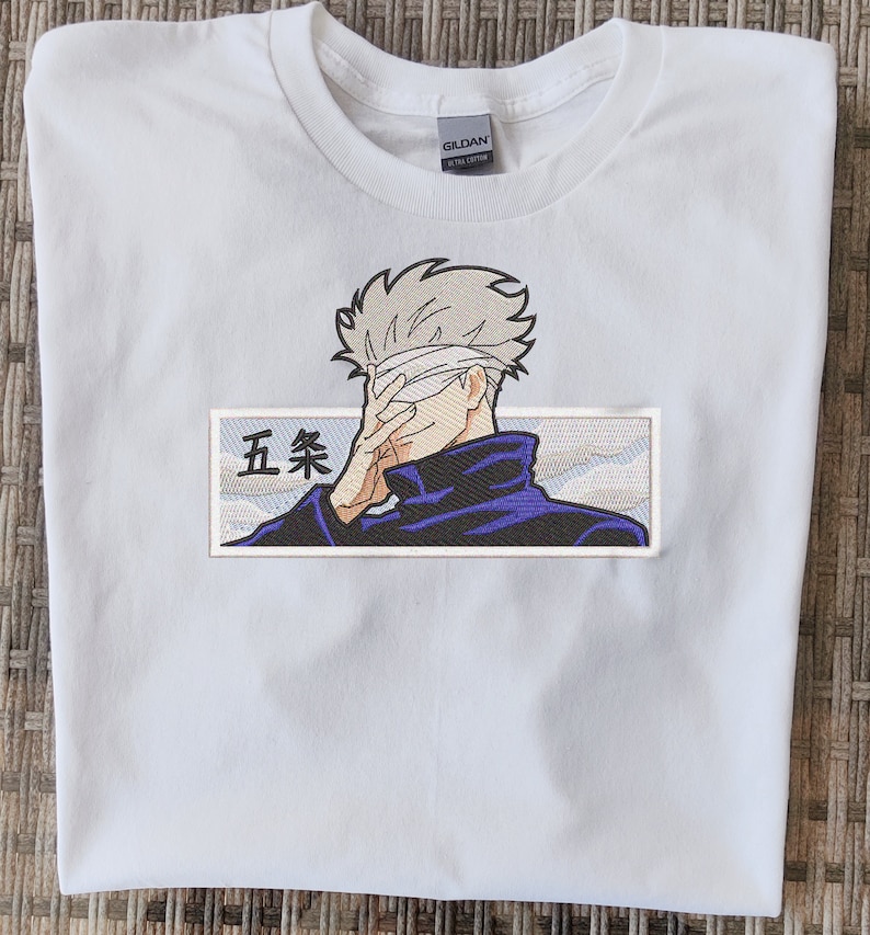 May include: White t-shirt with an embroidered patch featuring a character with a blindfold, a blue jacket, and the text "五条" in Japanese.