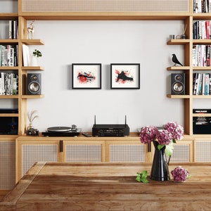 May include: A wooden bookshelf with a record player, amplifier, and speakers. The bookshelf is filled with books and has a woven cane panel on the bottom. There are two black framed abstract paintings on the wall above the record player.
