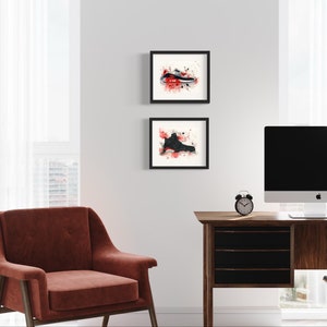 May include: Two framed black and white watercolor paintings of sneakers with red splatters on a white background. The paintings are hanging on a white wall above a wooden desk with a computer monitor, a chair, and a lamp.