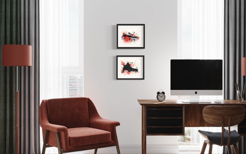 May include: Two framed black and white watercolor paintings of sneakers with red splatters on a white background. The paintings are hanging on a white wall above a wooden desk with a computer monitor, a chair, and a lamp.
