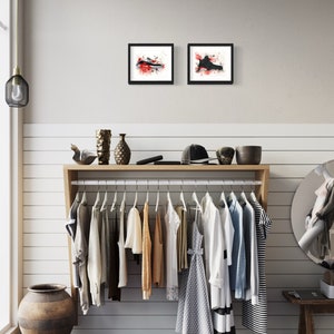 May include: A white wall with a wooden shelf holding a clothing rack with various clothing items hanging on it. There are two framed black and white watercolor paintings of sneakers on the wall above the shelf.