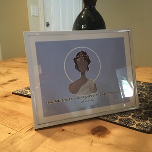 May include: A framed print with a light blue background featuring a drawing of a person with a laurel wreath on their head. The quote "The poets were always correct. I say, "You are of my soul." is printed below the drawing.