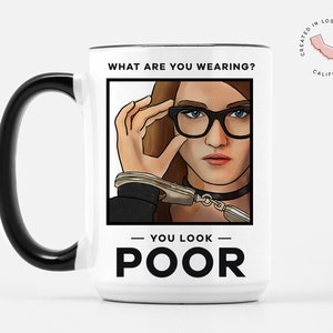 May include: White ceramic coffee mug with a black handle. The mug features a black and white illustration of a woman wearing glasses and handcuffs. The text "What are you wearing?" is above the illustration and "You look poor" is below the illustration.