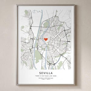 Puede incluir: Un mapa enmarcado de Sevilla, España, con fondo blanco, calles negras y zonas verdes. Un corazón rojo marca una ubicación central. El texto dice SEVILLA, THERE IS NO PLACE LIKE HOME, Plaza Nueva, 1, 41001 Sevilla, España, 37.3887 N - 5.98437 W.