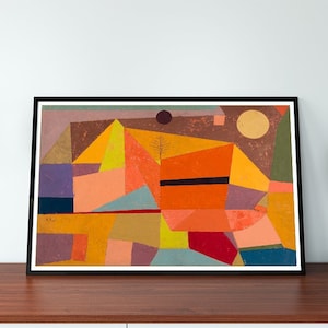 May include: Abstract geometric art print in a black frame with a variety of colors including orange, yellow, red, purple, and blue. The print is hanging on a white wall above a wooden table.