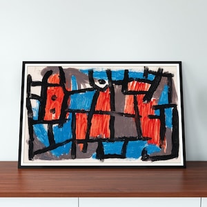 Puede incluir: Pintura abstracta en un marco negro con líneas y formas rojas, azules y negras sobre fondo blanco. La pintura está sobre una mesa de madera con una lámpara negra y un altavoz negro.