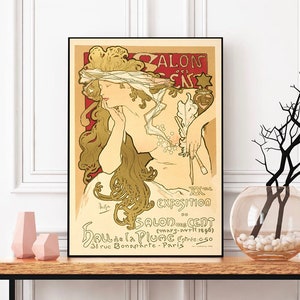 Peut inclure: Une affiche vintage annonçant l'exposition du Salon des Cent, mettant en scène une femme en robe fluide tenant une plume et un pinceau. Le texte indique "Salon des Cent (mars-avril 1896) Hall de la Plume Entre 36 rue Bonaparte - Paris".