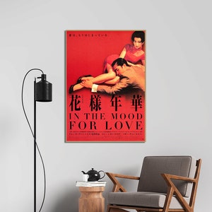 Puede incluir: Un p&oacute;ster de pel&iacute;cula rojo y dorado para la pel&iacute;cula "In the Mood for Love" que presenta a una pareja en un abrazo rom&aacute;ntico. El p&oacute;ster incluye el t&iacute;tulo de la pel&iacute;cula en ingl&eacute;s y japon&eacute;s, as&iacute; como los nombres del director y los actores.