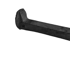 Puede incluir: Un clavo de vía negro, un gran sujetador de metal forjado. Tiene un vástago rectangular y una cabeza en un extremo. El clavo está diseñado para asegurar los rieles a las traviesas de madera. El objeto está aislado sobre un fondo blanco.