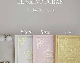 May include: Three hardcover copies of "Le Saint Coran" in Arabic and French. The books are bound in white, pink, and gold.