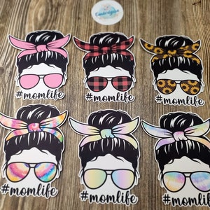 Peut inclure: Six autocollants diff&eacute;rents sur le th&egrave;me de la vie de maman avec une femme portant un chignon d&eacute;sordonn&eacute; et des lunettes de soleil. Chaque autocollant a un motif diff&eacute;rent sur le bandeau et les lunettes de soleil. Le texte #momlife est sous chaque autocollant.