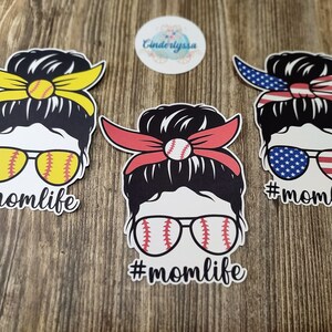 Peut inclure: Trois autocollants en vinyle repr&eacute;sentant une femme de dessin anim&eacute; avec un chignon d&eacute;sordonn&eacute;, des lunettes de soleil et un bandeau. Les bandeaux sont jaunes, rouges et rouge, blanc et bleu. Les lunettes de soleil sont d&eacute;cor&eacute;es d'un motif de baseball. Chaque autocollant porte le texte "#momlife" sous le dessin anim&eacute;.