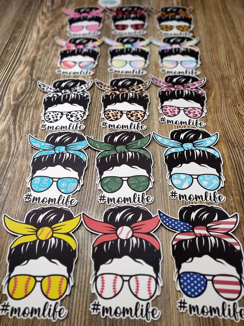 Peut inclure: Un ensemble de 12 autocollants en vinyle color&eacute;s repr&eacute;sentant une femme de dessin anim&eacute; avec un chignon d&eacute;sordonn&eacute;, des lunettes de soleil et un bandana. Chaque autocollant porte le texte "#momlife" sous l'image. Les bandanas sont de motifs diff&eacute;rents, notamment des imprim&eacute;s l&eacute;opard, floraux et &agrave; carreaux.