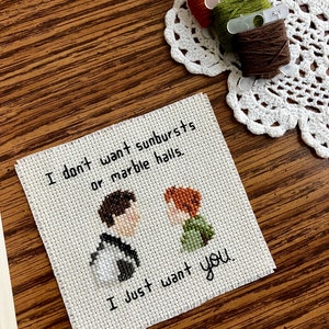 May include: Cross-stitch embroidery on white fabric with the text "I don't want sunbursts or marble halls. I just want you."